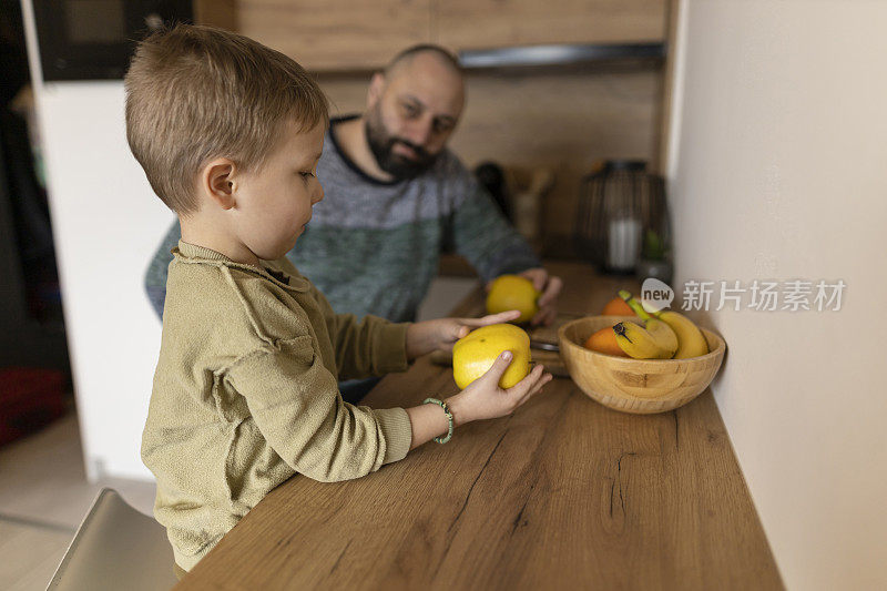 父亲和孩子在厨房分享食物。温暖的联系，美丽的自然光线下充满希望的情感。吃他们最喜欢的水果苹果和橘子。健康的生活方式，亲密的时间。