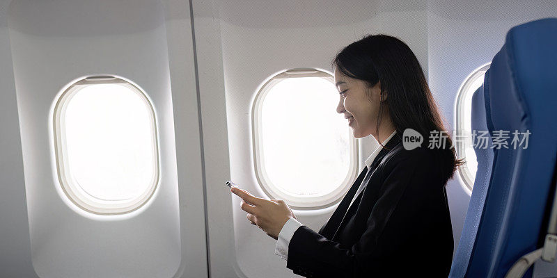 亚洲年轻的成功女企业家或女企业家在飞机上穿着正装，坐在商务舱的座位上，在飞行中使用智能手机。旅游与商务理念