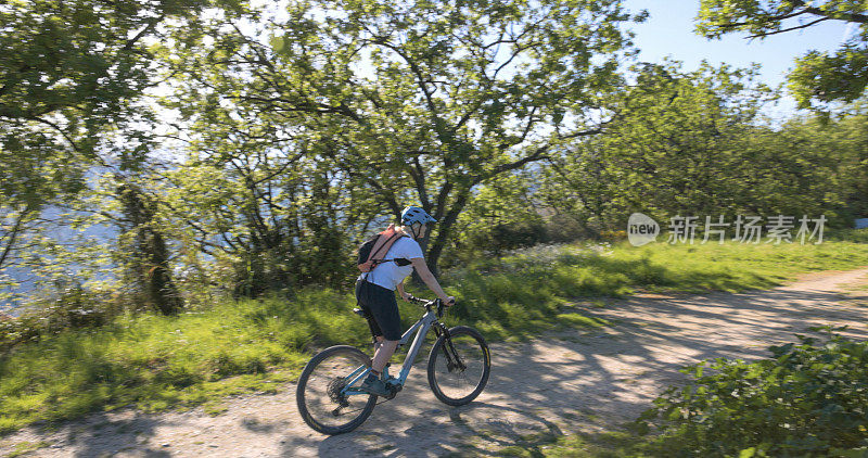 成熟的女人骑着电动自行车在森林的小路上行驶