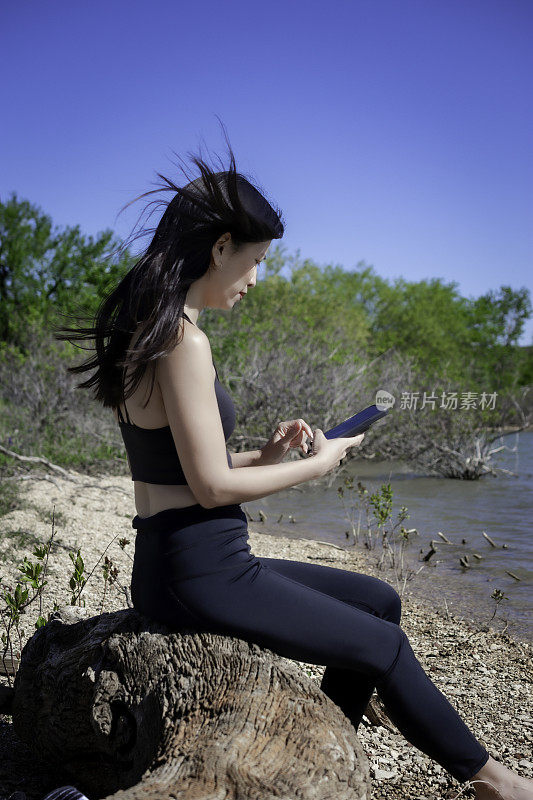 一名女子在用手机锻炼后坐在浮木上