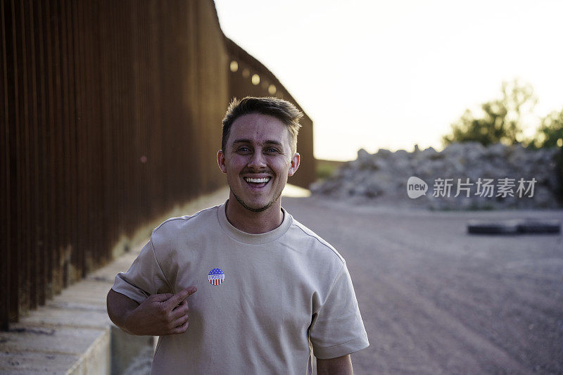 黄昏时分，一名年轻人站在美国德克萨斯州和墨西哥奇瓦瓦州华雷斯之间的国际边境墙前，身上贴着“我投了美国票”的贴纸