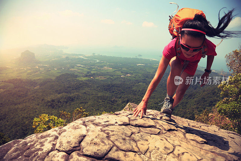 年轻的亚洲女子徒步旅行者攀登岩石的山峰悬崖