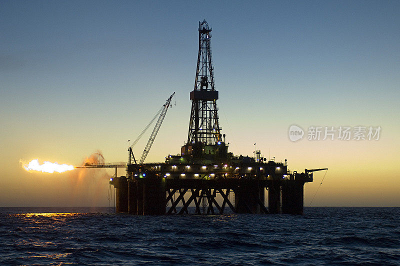 日落时海洋石油钻井平台的剪影。