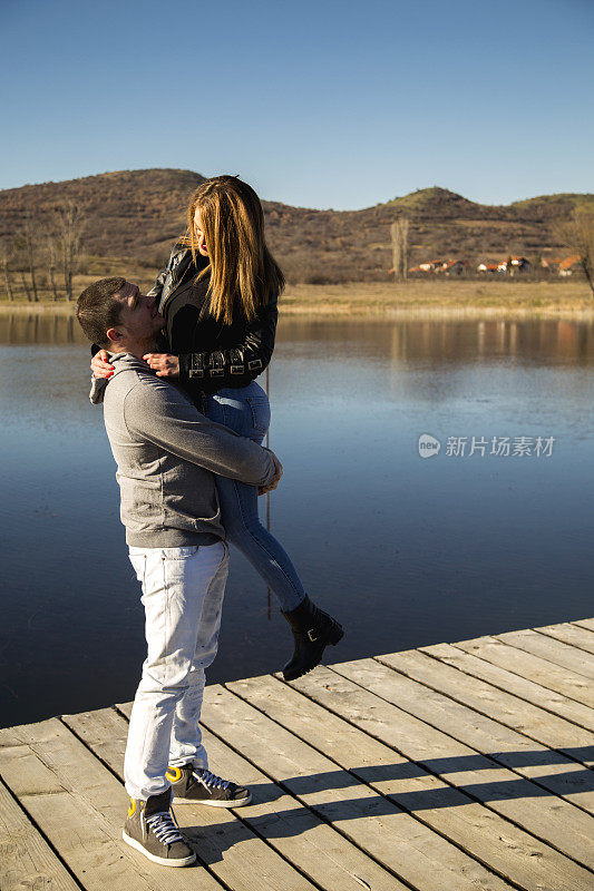 一对男情侣坐在湖边的木码头上接吻