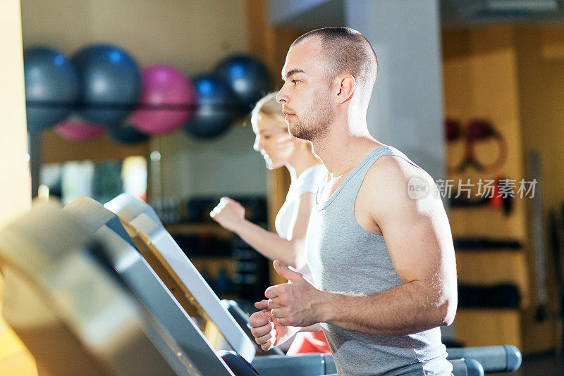 两个白人运动员在健身房的跑步机上热身