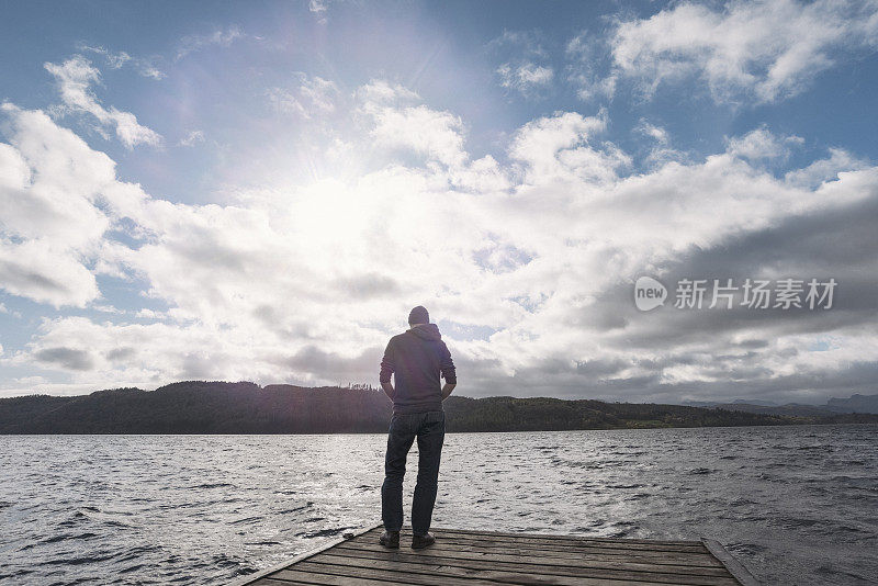 一个男人站在防波堤的尽头俯瞰着一个湖。