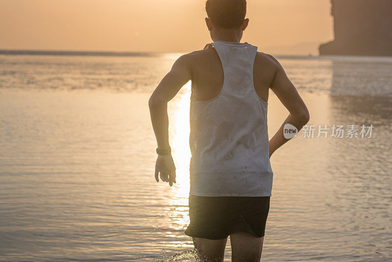 年轻的亚洲男子在海滩上奔跑，夕阳为背景