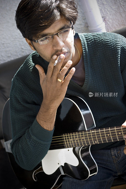 一个抽烟的印度青年，拿着一把吉他的竖像