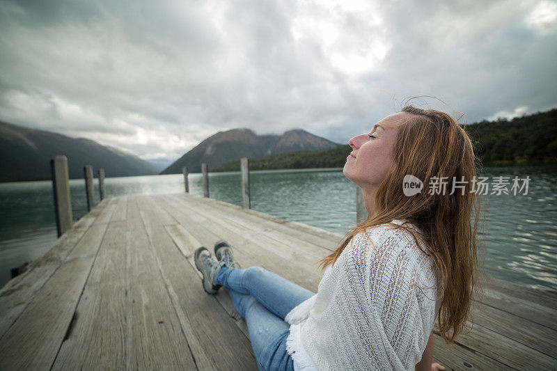 快乐的年轻女子在湖码头上休息