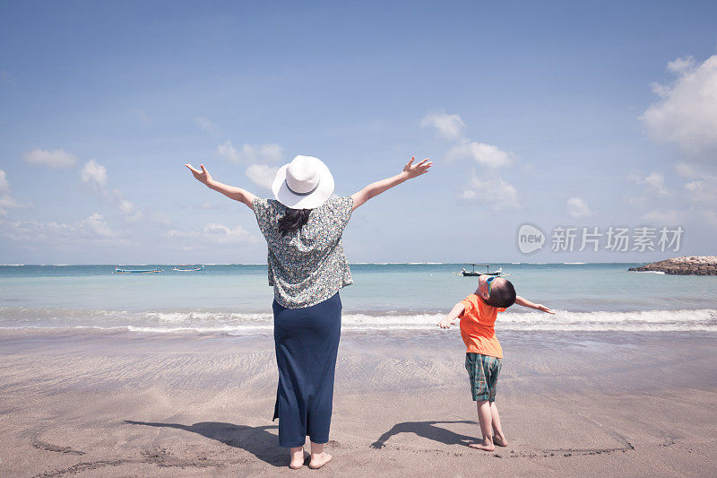 母亲和儿子在海滩上张开双臂