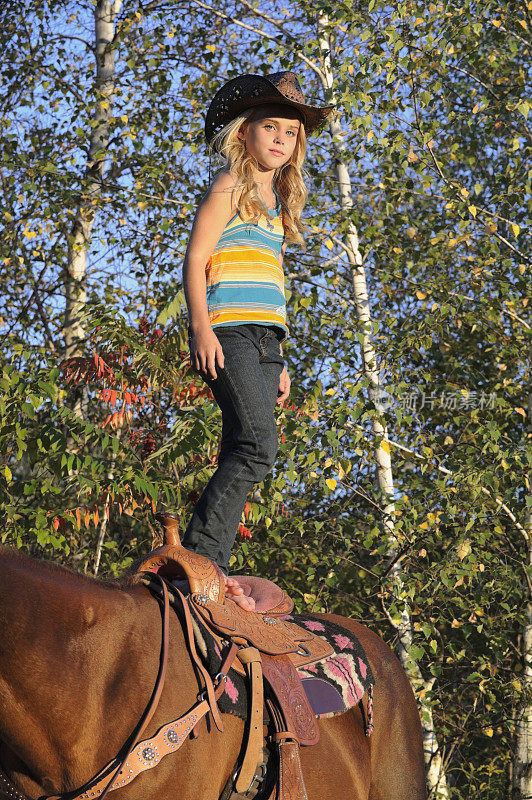 年轻的金发女牛仔站在她的马鞍上，自信