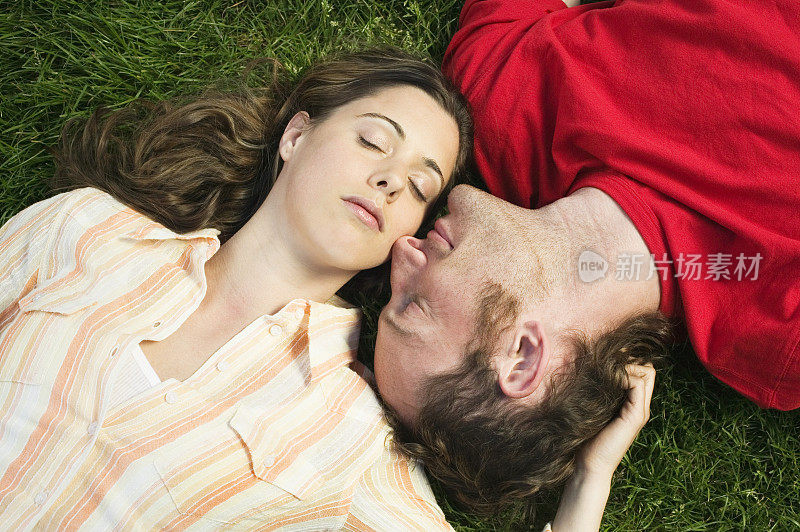 一对年轻夫妇头挨着头躺在草地上
