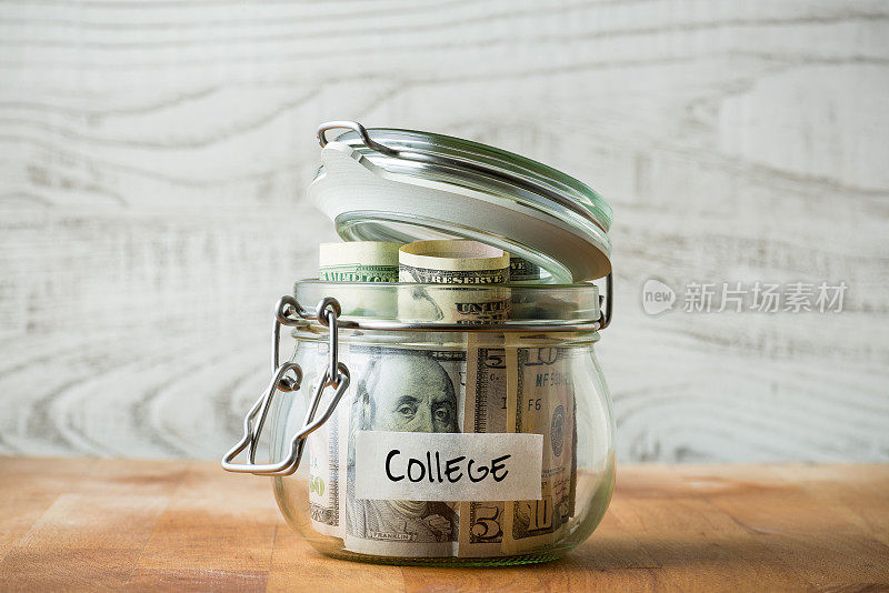 在木制背景上孤立的玻璃罐中的美元。为上大学存钱。