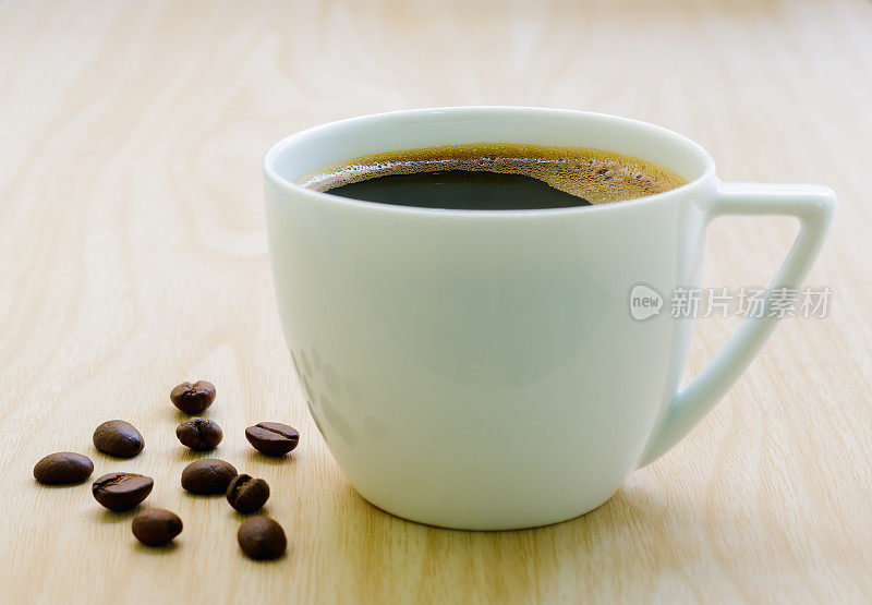 木桌上的咖啡杯和咖啡豆。黑咖啡，白色陶瓷杯，特写。