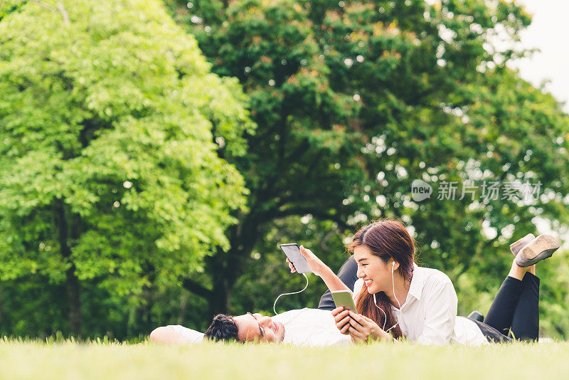 年轻的亚洲可爱的夫妇或大学生一起在花园里听音乐，与拷贝空间。休闲活动，爱情关系，婚礼，或放松休闲的生活方式概念