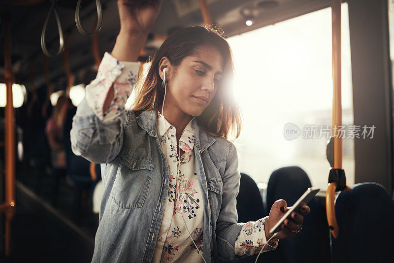 年轻女子站在公共汽车上听音乐