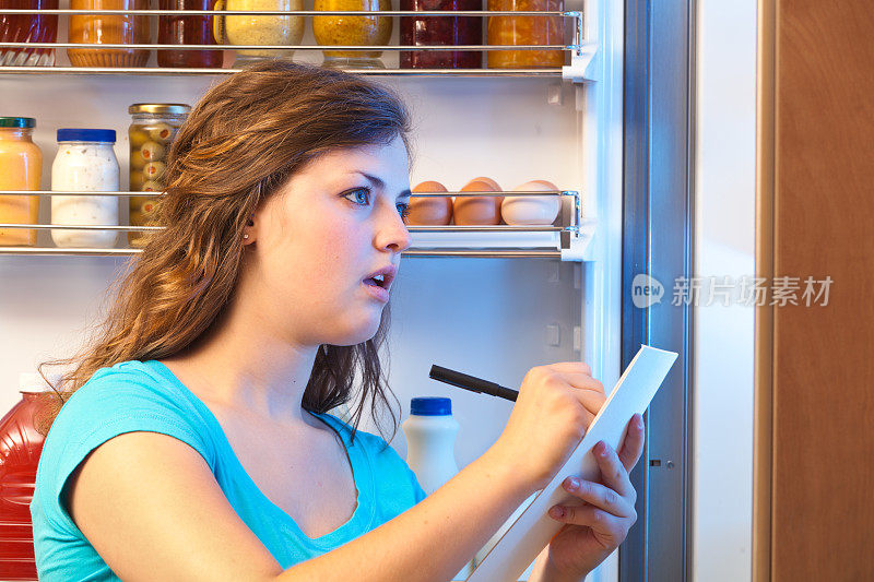 女人在冰箱前制作食品采购清单