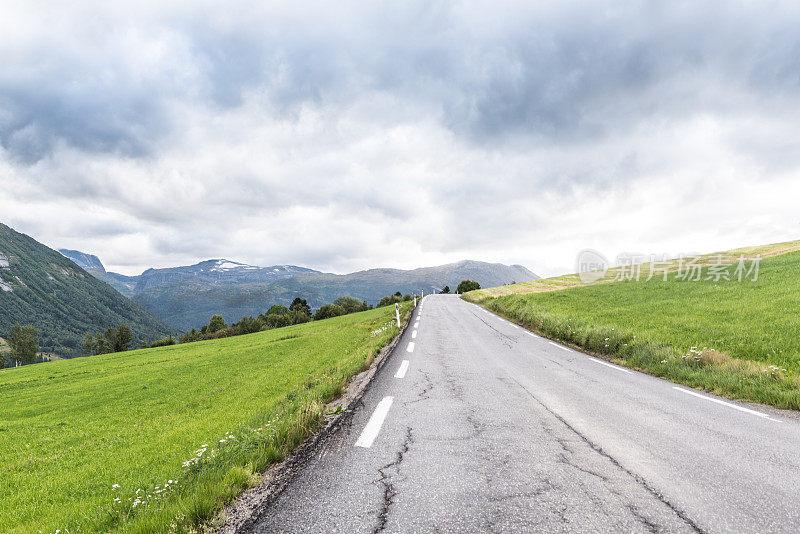 笔直的柏油路穿过挪威绿色的草甸山丘