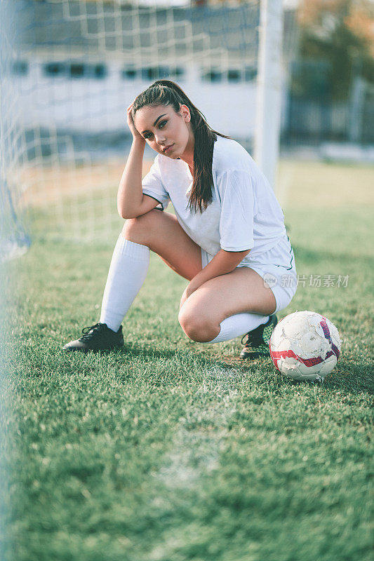 可爱的女足球运动员摆姿势跪着