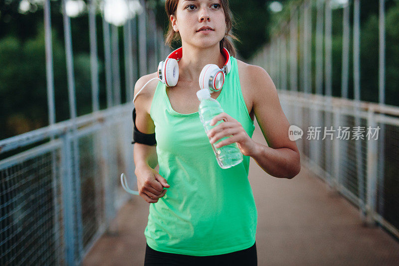 慢跑女孩拿着水瓶在户外跑步