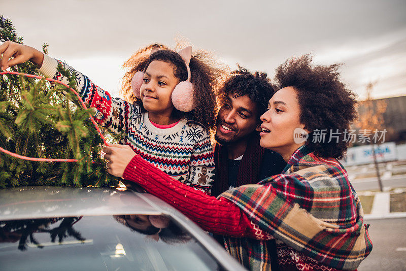 快乐的家庭和一个孩子把圣诞树放在车上
