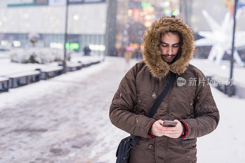 一个年轻人在一个下雪天后在城市发短信。