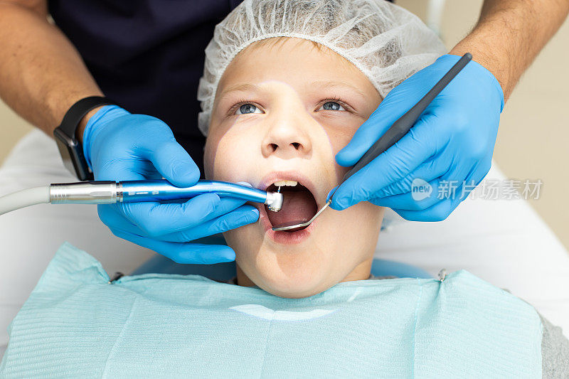 小男孩躺在牙医的椅子上，让专业的口腔医生给他的牙齿钻孔