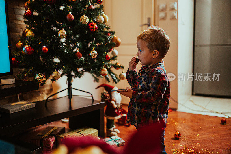 蹒跚学步的小男孩在圣诞节期间使用手机和看电视