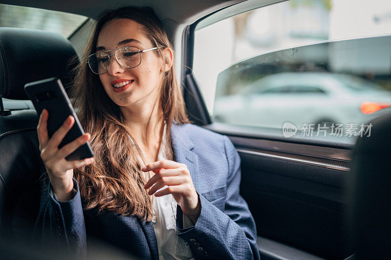 女商人坐在汽车后座上使用智能手机