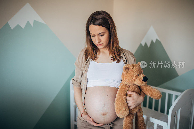 孕妇在婴儿的卧室里抱着泰迪熊