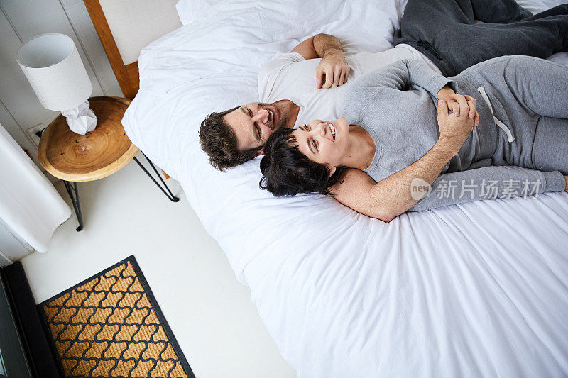 清晨，一对微笑的年轻夫妇躺在他们的床上