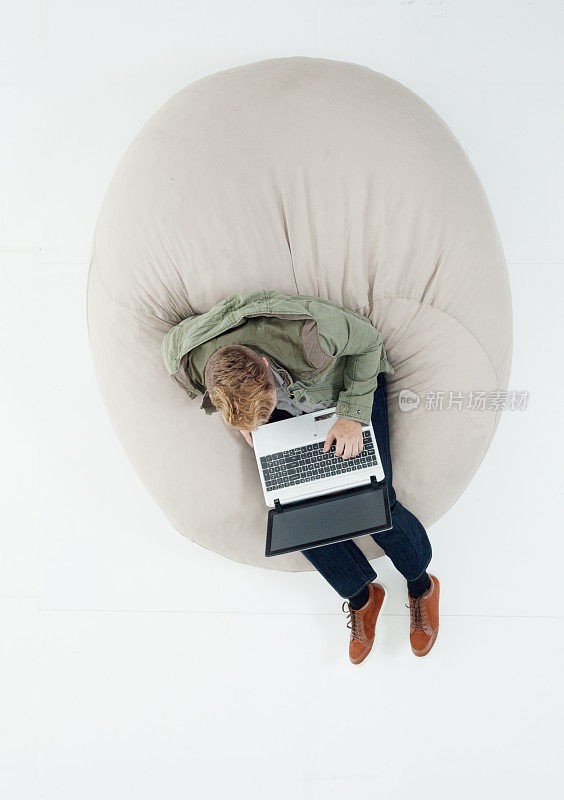 白人男孩穿着牛仔裤在白色背景前休息，使用笔记本电脑