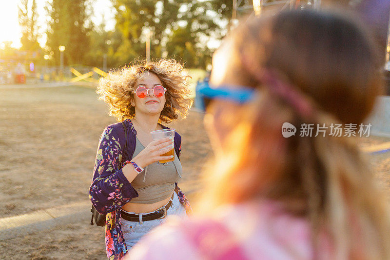 年轻女子拿着啤酒杯跳舞，看着她的朋友在户外活动