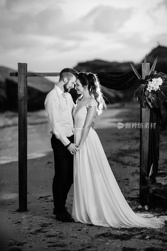 年轻的新郎和新娘晚上在海滩上捧着一束花