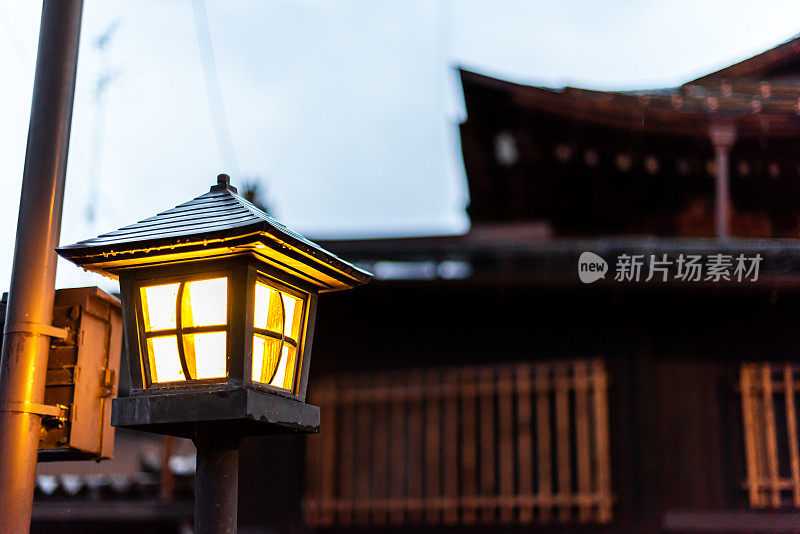 在日本岐阜县高山，一盏传统木制灯灯，背景是町屋排屋，在晚上的夜晚