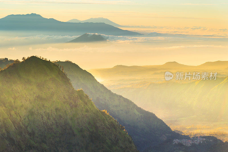 色彩斑斓的风景与高火山山，美丽的绿色弯曲森林日落天空与云彩和黄色的阳光在夏季日落在印度尼西亚