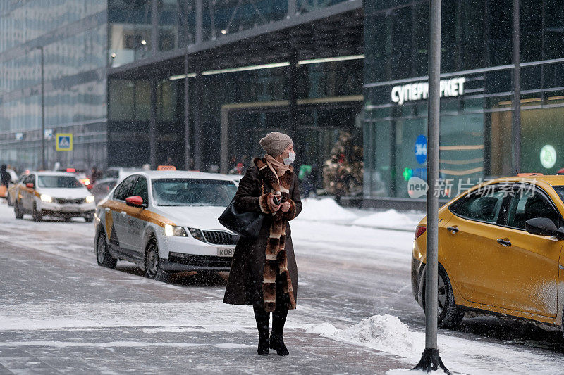 一个女人在冬天走在街上，下着雪。
