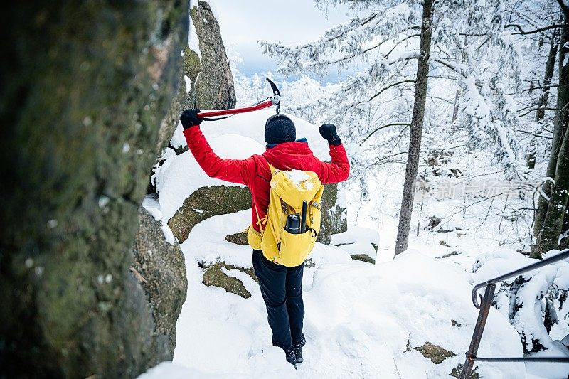 快乐的攀岩者穿着红色羽绒服拿着冰斧。冬季活动。