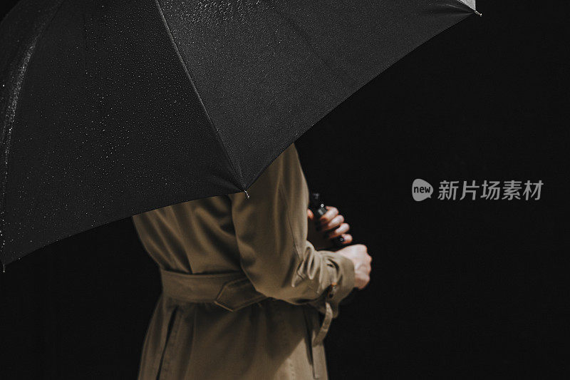 身着雨衣，拿着一把打开的黑伞的匿名女子(摄影棚拍摄)