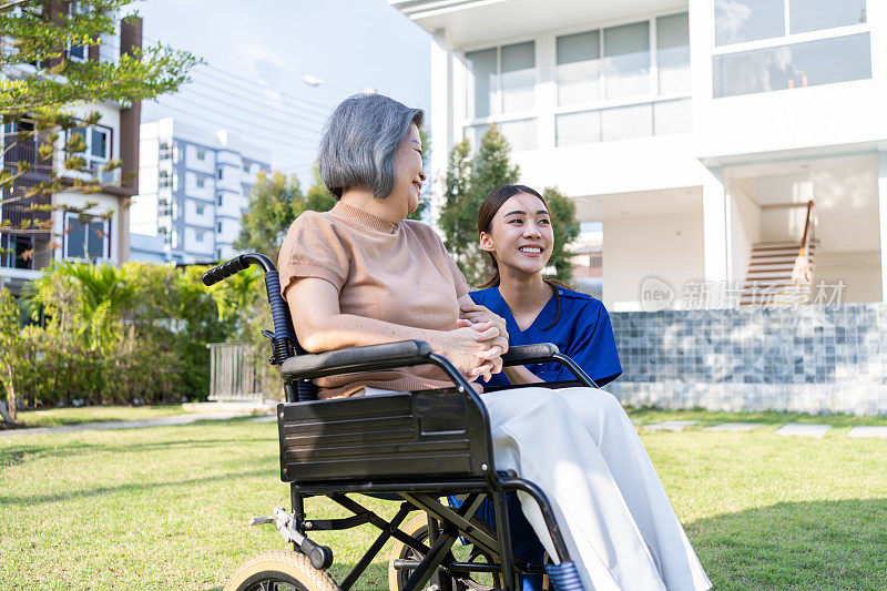 亚裔护理人员在户外照顾坐轮椅的残疾老妇人。美丽的女孩医生帮助和照顾在公园养老院做物理治疗的老年残疾患者。