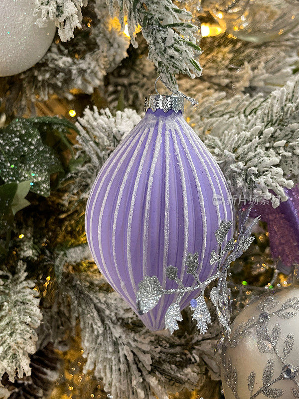 个人形象，手风琴效果，淡紫色，泪滴状的小饰物挂在人造圣诞树的树枝上，云杉针覆盖着人造雪花，模糊的白色精灵灯背景