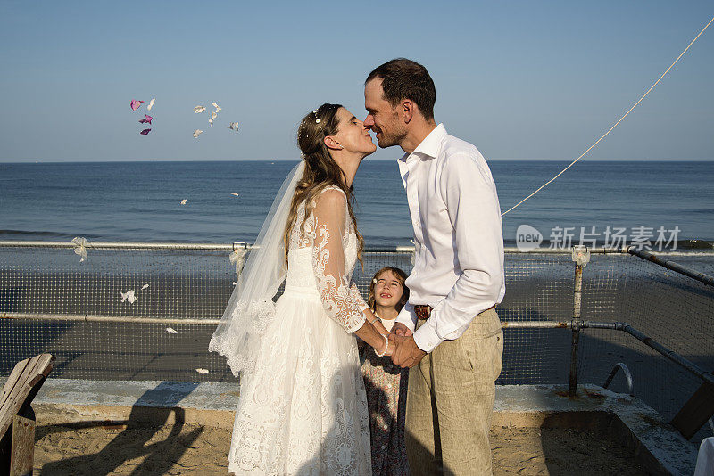 新婚夫妇在海滩小屋的玫瑰花瓣下接吻。