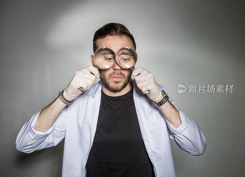 身穿白大褂的年轻男医生把放大镜放在牙齿前微笑着。医疗保健中的幽默概念。
