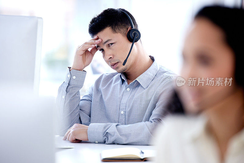 一个年轻的呼叫中心职员在办公室的电脑前工作时看起来压力很大