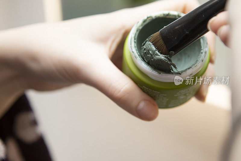 特写手握刷子和绿色面膜的罐子