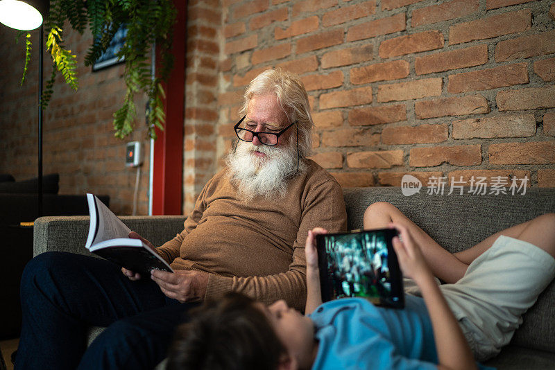 爷爷在家看书，孙子在家用平板电脑