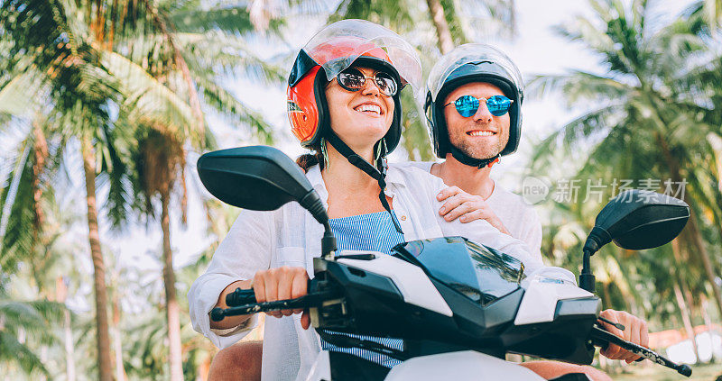 在泰国苏梅岛的棕榈树下，一对带着安全帽骑着摩托车的幸福微笑的情侣在热带度假