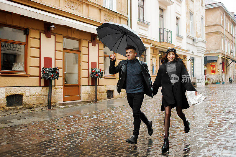 漂亮的一对在雨天跑在街上。那个人手里拿着一把伞。2019年11月2日，乌克兰利沃夫。