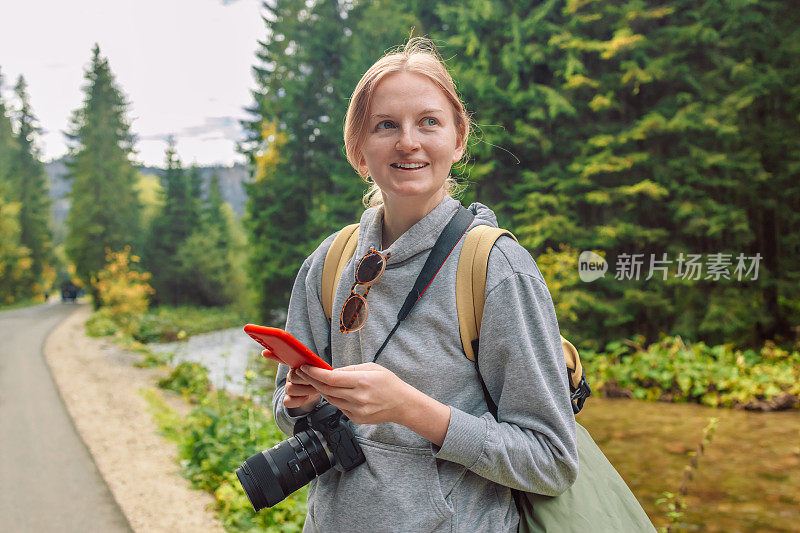 年轻女子在夏天远足时在树林里散步时使用手机。秋天在森林里远足。在大自然中冒险。积极的生活方式