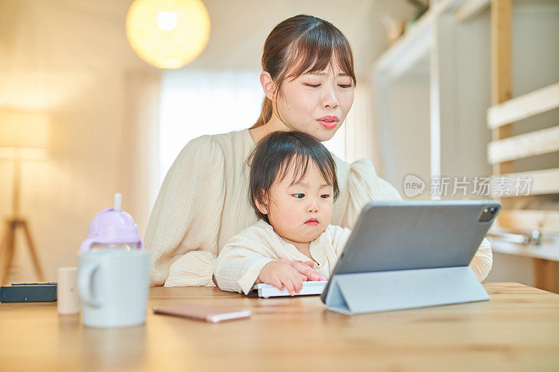 摆弄着平板电脑的女人和婴儿，脸上带着疲惫的表情